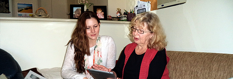 photo of Home Library Service volunteer sitting with a client on a home lounge looking at iPad